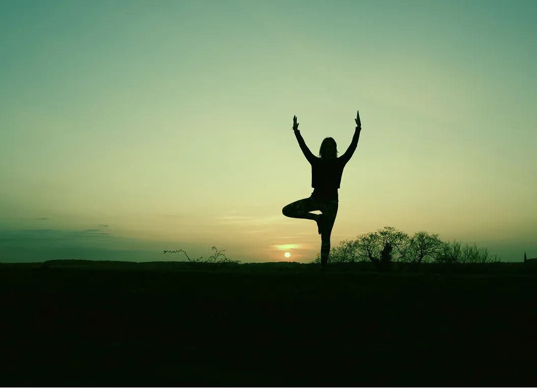 Une personne en posture de yoga face au soleil levant.